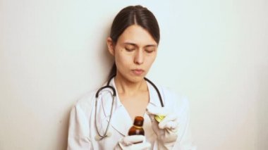 Doktor, tek kullanımlık lastik eldivenli bir kadın bir dezenfektan alır ve ellerini tedavi eder, tek kullanımlık bir şırınga alır ve gerekli ilacı şırınganın içine sokar.