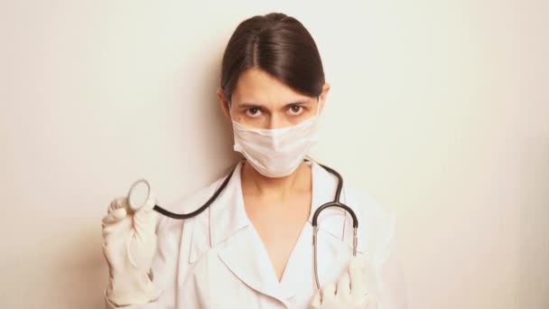 白い使い捨ての保護マスクと使い捨て手袋の女性医師は聴診器を取り出し患者の話を聞く準備をします — ストック動画