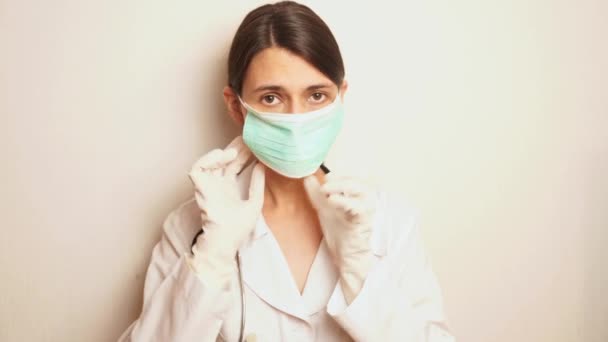 女性セラピストは青い使い捨ての保護マスクを顔につけ綿のウールを一枚取り消毒剤を注射し白いゴム使い捨て手袋で手を治療します — ストック動画