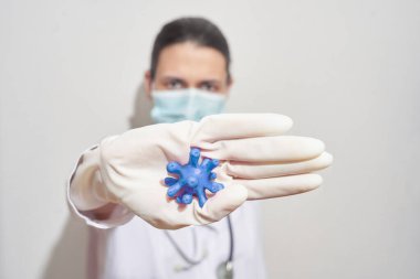  Tek kullanımlık tıbbi maskeli genç bir kadın enfeksiyonu durdurmak için el kol hareketi yapıyor elinde bir virüs tutuyor, küresel bir salgın.                                 