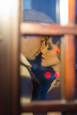 Genç bir adam kadınını kucaklıyor ve onu öpmek istiyor. Cam kapıların arkasındalar. Hem de retro kıyafetlerle. Tarihi yeniden yapılandırma