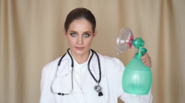 Kadın bir doktor kameraya bakar ve solunum cihazını gösterir, elleriyle bir haç gösterir ve kafasıyla hayır der, sonra evi işaret eder. Evde oturma konsepti, karantina, solunum cihazı.