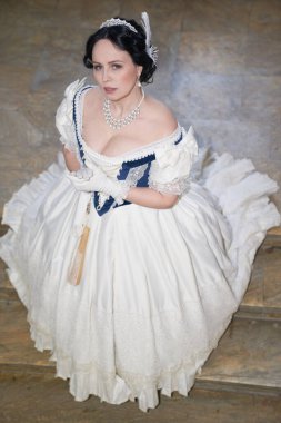 Güzel bir kız, düşük yakalı, eski tarz, siyah saçlı, beyaz tüylü romantik bir elbise giyiyor. Uzundu, merdivenlerde dikilip kameraya bakıyordu. Tarihi yeniden yapılandırma                               