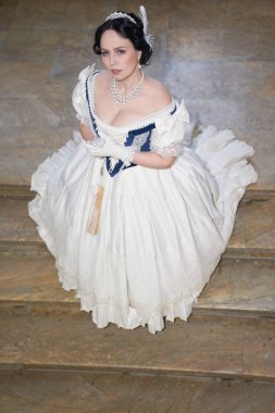 Güzel bir kız, düşük boyunlu, eski tarz, siyah saçlı, beyaz tüylü romantik bir elbise giyiyor. Uzundu, merdivenlerde duruyordu ve başka tarafa bakıyordu. Tarihi yeniden yapılandırma                                 