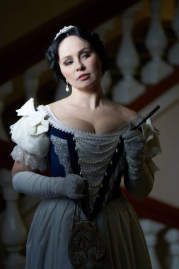  Güzel bir kızın portresi romantik bir elbise içinde, eski moda bir tarzda. Koyu renk saçlı. Duvara yaslanmış, tırabzanın yanında tüfeğini tutuyor. Başka tarafa bak. Tarihi yeniden yapılandırma                               