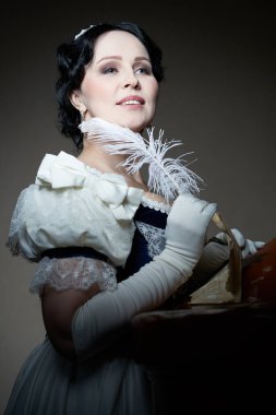  Güzel bir kız, romantik bir elbise içinde, eski moda. Koyu renk saçlı. Tiyatroda sahnenin arka planına karşı dimdik ayakta duruyor ve kafasını çeviriyor. Tarihi yeniden yapılandırma                               