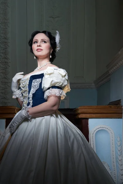 Beautiful girl, in a romantic dress, retro style.With dark hair. He stands in full height, against the background of the stage in the theater, and looks away. Historical reconstruction
