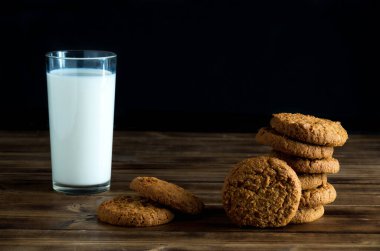 Tahta yüzeyde yulaf değirmenli kurabiye ve süt bardağı yığını