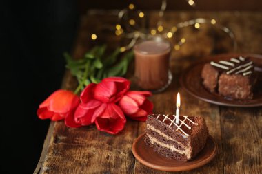 Kırmızı çiçekler, mumlu pasta ve ahşap masada bir içki..