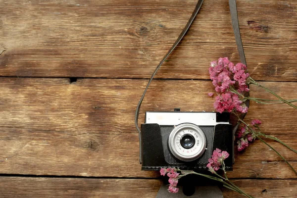 On a wooden table is a camera with flowers.