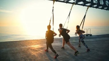 Sportif insanlar ağız kavgası trx güneş karşı deniz kenarında ile eğitim. Ağır çekim.