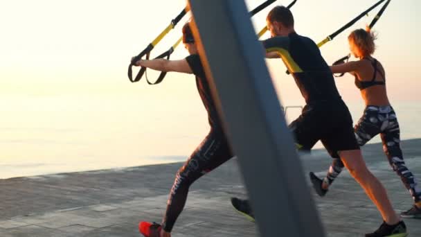 Mooie sportieve mensen trainen met trx aan zee bij zonsopgang. Slow motion. — Stockvideo