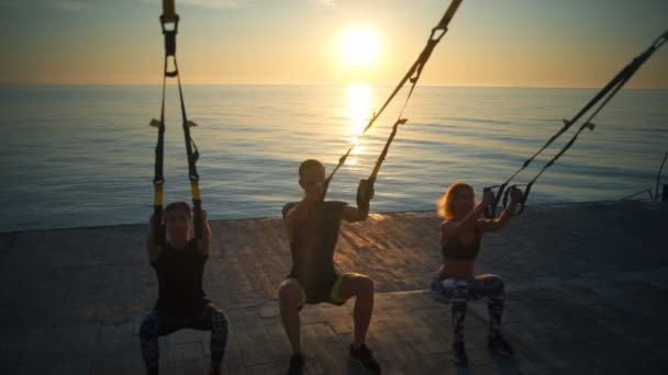 Silhouetten von Sportlern, die bei Sonnenaufgang Kniebeugen mit Trampolin trainieren. Zeitlupe. — Stockvideo