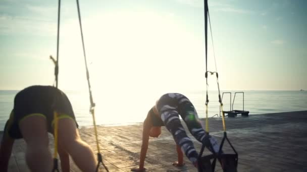 Rückansicht von 3 Personen trainieren mit trx in Meeresnähe in Zeitlupe — Stockvideo