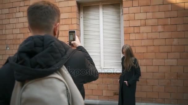 Um homem tirando uma foto de uma jovem mulher bonita com um smartphone câmera lenta — Vídeo de Stock