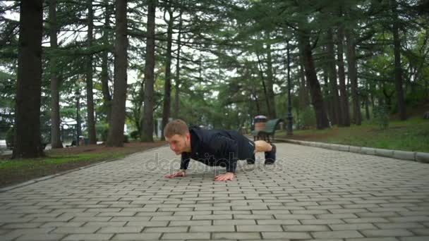 Ung man med hälsosam livsstil gör push ups i city park slow motion — Stockvideo