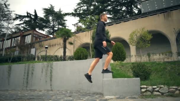 Un joven guapo haciendo un paso adelante con ejercicio de rodilla alta al aire libre — Vídeo de stock