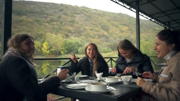 Mladí veselé ženy jíst v restauraci na terase u rybníka — Stock video