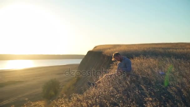 Hombre y perro sentados al borde del precipicio al atardecer — Vídeos de Stock