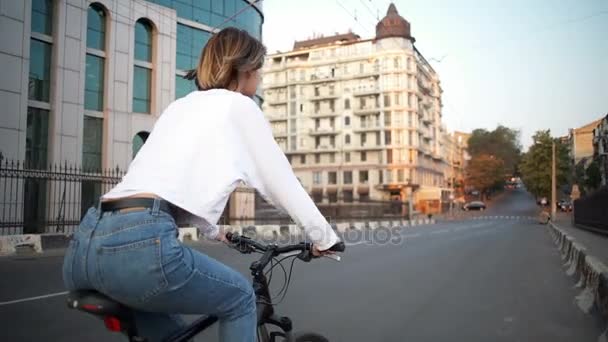 Νεαρή γυναίκα βόλτες με ένα ποδήλατο που χαμογελά στη φωτογραφική μηχανή στο άδειο δρόμο — Αρχείο Βίντεο