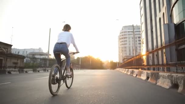 Frau fährt bei Sonnenaufgang mit Fahrrad die leere Straße hinunter — Stockvideo