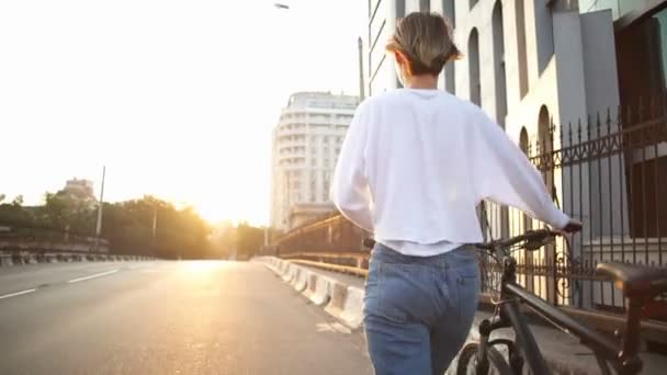 Back view mulher caminha pela rua carregando sua bicicleta — Vídeo de Stock