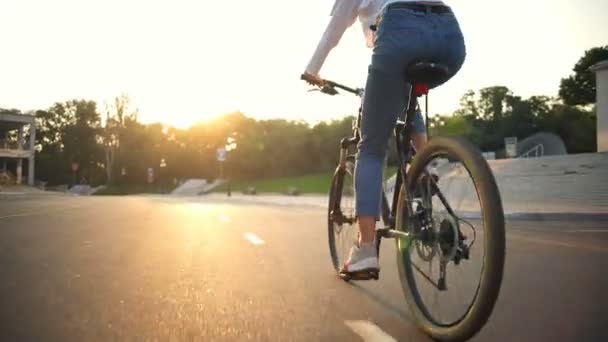 Bakifrån ung kvinna rider en cykel genom parken i solljus — Stockvideo