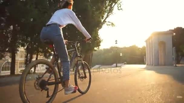 ΠΙΣΩ ΟΨΗ γυναίκα, ιππασία, ποδήλατο μέσω του πάρκου στο φως του ήλιου — Αρχείο Βίντεο