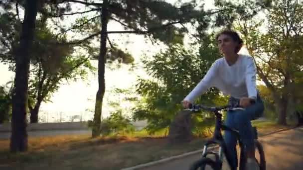 Atraente feliz fêmea monta uma bicicleta através do parque no dia ensolarado — Vídeo de Stock