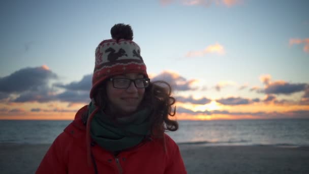 Μια όμορφη χαμογελαστή νεαρή γυναίκα που φοράει γυαλιά στην Ανατολή του ηλίου στην παραλία — Αρχείο Βίντεο