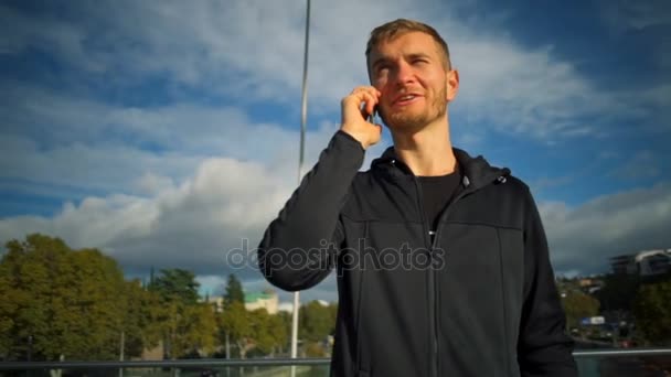 Mladý muž mluvil po telefonu a usmívá se na krásný most Zpomalený pohyb — Stock video