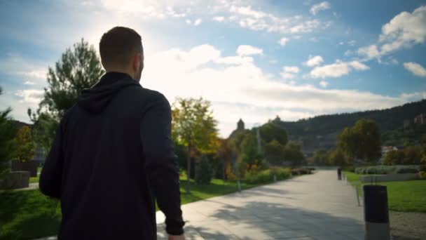Un hombre joven en forma con auriculares corriendo en un hermoso parque de cámara lenta — Vídeos de Stock