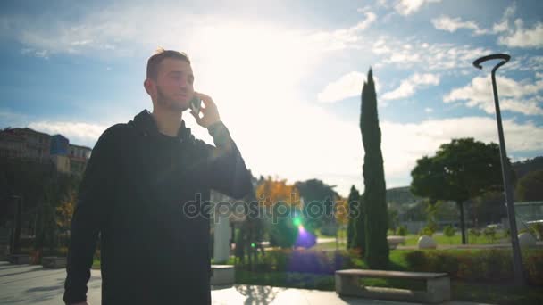 A young man walking in a beautiful park and talking on the phone slow motion — Stock Video