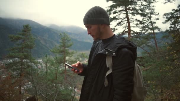 Молодий красивий чоловік стоїть в лісі і використовує свій смартфон повільний рух — стокове відео