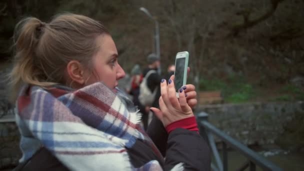 Μια νεαρή όμορφη γυναίκα, λαμβάνοντας μια φωτογραφία με το smartphone στη γέφυρα — Αρχείο Βίντεο