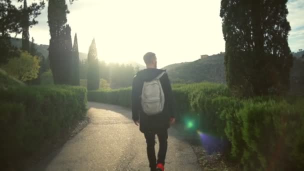 Ung man med en ryggsäck som promenader i en vacker park slow motion — Stockvideo