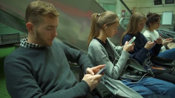Junge Reisende mit Taschen und Smartphones sitzen und warten am Flughafen — Stockvideo