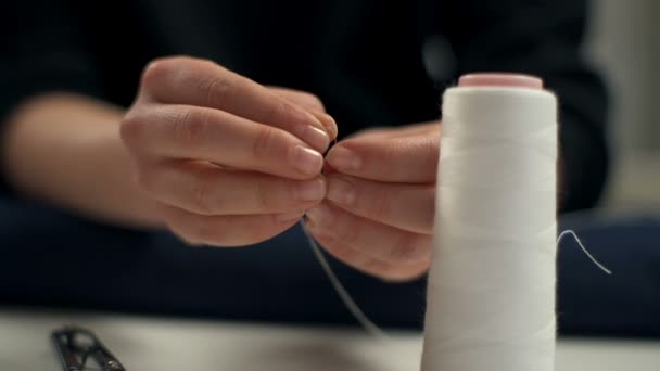 Costurera enhebrando la aguja con hilo medio blanco doblado en el taller — Vídeo de stock