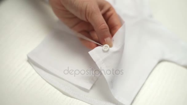 Young woman accurately sewing buttons on the white tiny shirt in the workshop — Stock Video