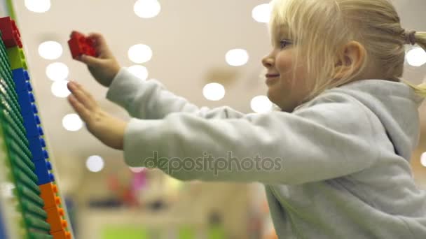 Menina llittle bonito coloca um cubo de lego no tabuleiro no playground câmera lenta — Vídeo de Stock