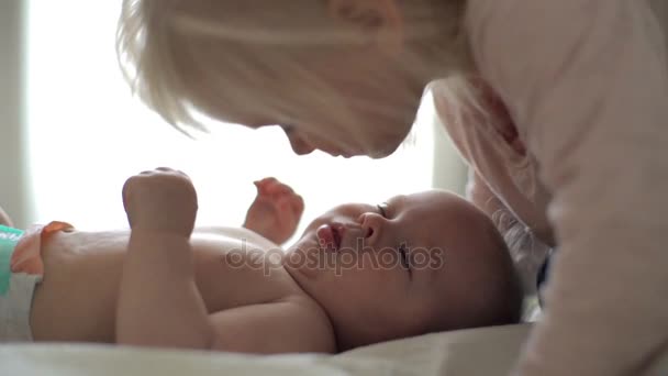 Девушка целует милого ребенка в постели, а потом улыбается замедленной съемке. — стоковое видео