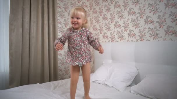 Beautiful blonde girl jumping on the bed and smiling slow motion — Stock Video