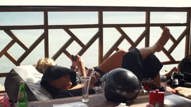 Група людей, що лежать на терасі зі своїми телефонами — стокове відео