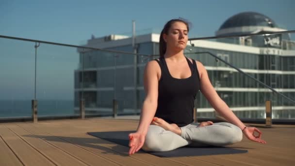 Junge attraktive Frau meditiert auf dem Dach auf See Zeitlupe — Stockvideo
