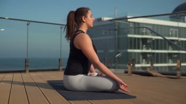 Молодая привлекательная женщина медитирует на крыше в море замедленным движением — стоковое видео
