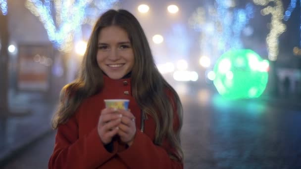Молодая привлекательная женщина стоит на улице с чашкой кофе замедленной съемки — стоковое видео