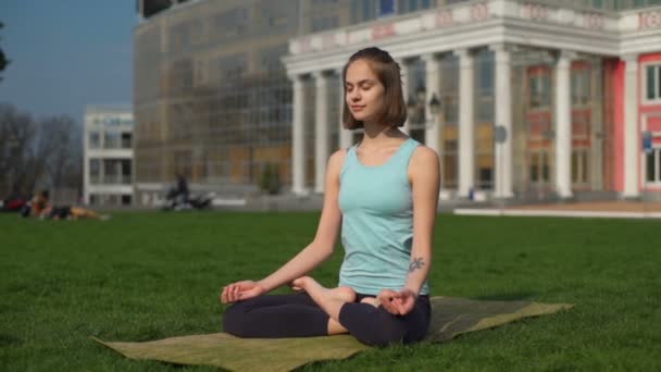 Молода струнка жінка сидить на килимку в позі лотоса і медитує повільний рух — стокове відео