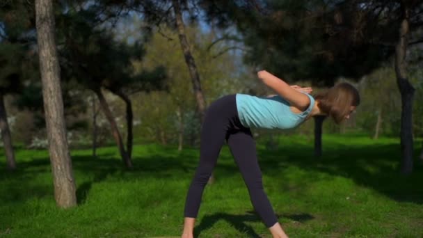 Ung smal kvinna gör yoga på gräsmattan i parken slow motion — Stockvideo