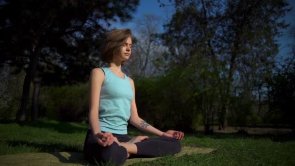Ung smal kvinna sitter i lotus pose och koppla av på gräsmattan i parken slow motion — Stockvideo