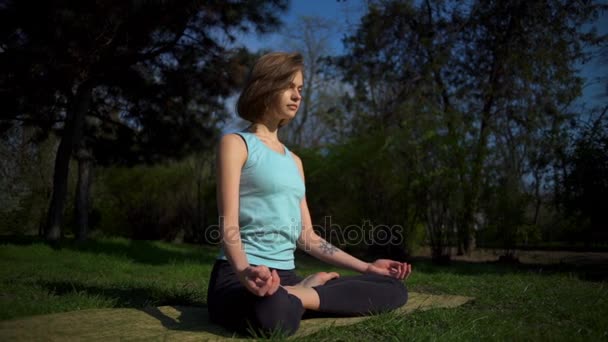 Joven hembra delgada haciendo namaste después de la pose de loto en el césped en cámara lenta parque — Vídeos de Stock